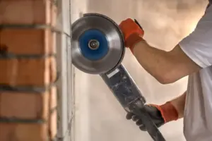 Industriebauer arbeitet mit einem professionellen Winkelschleifer, um Ziegel zu schneiden